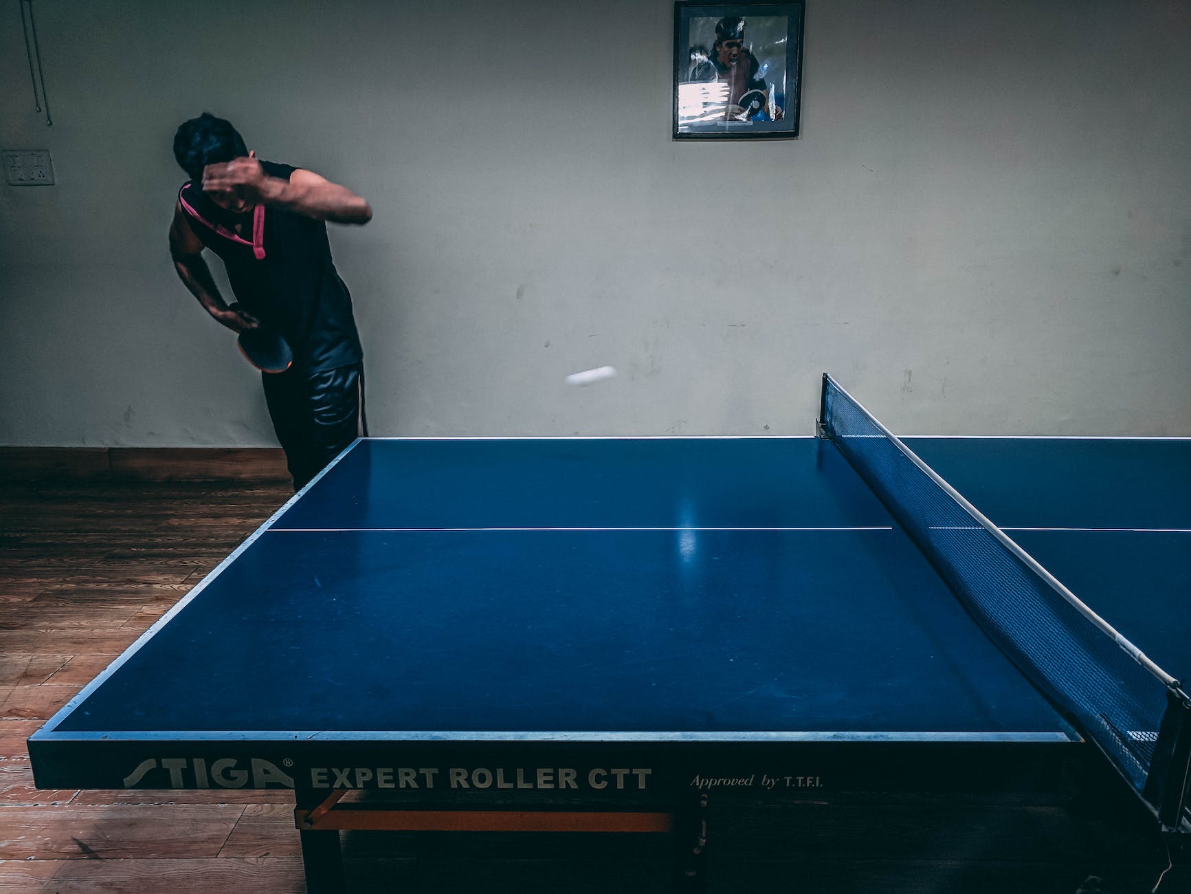 man in black shirt standing near blue wooden pingpong table